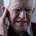 Photo of elderly man with painful expression on his face, holding fingers to his ear